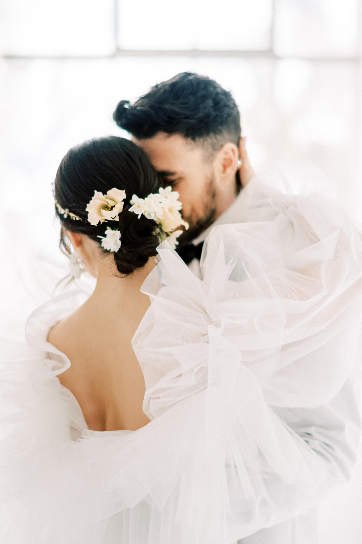 Fine art white on white themed stylish and elegant wedding captured on film - bride is wearing a tulle and chantilly lace Monique Lhuillier custom made bespoke wedding dress; fresh seasonal spring flowers to accentuate the half up do French chignon bridal hairstyle; groom has a clean cut and is wearing a white Dior tuxedo; backdrop is a big white bay window style similar to Chateau de Villette - Photo by London based destination wedding photographer Cristina Ilao